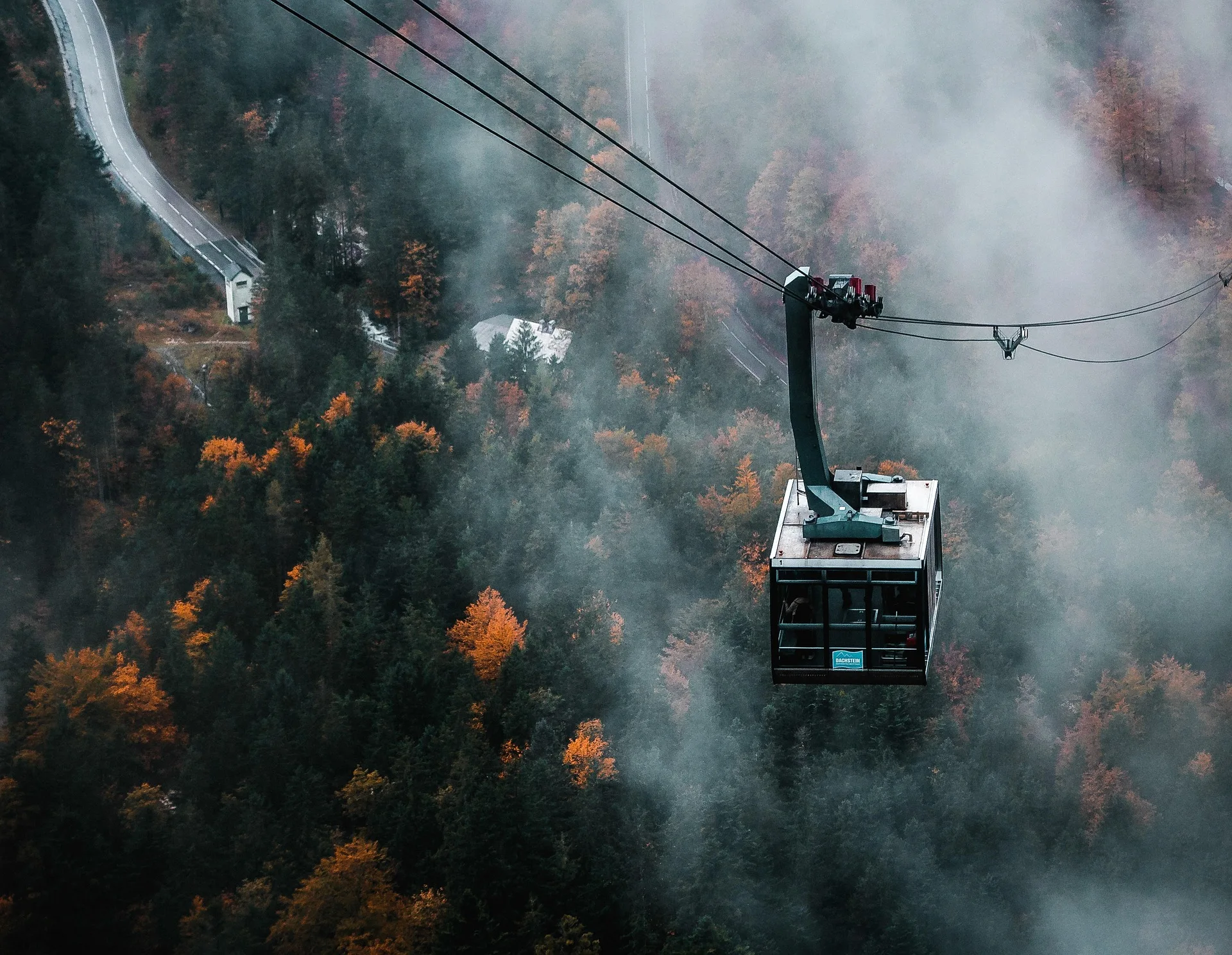 Aerial view of a gondola crossing over a foggy forest during autumn.